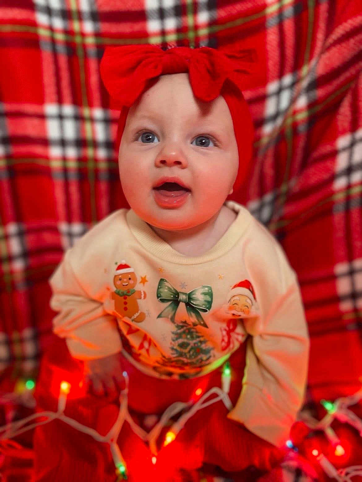 Harper is registered to the contest to win money with this photo: baby, child, red_bow, headband, christmas_lights, festive_sweater, gingerbread_man, christmas_tree, santa_claus, plaid_blanket, holiday, indoors, cute, smiling, happy, portrait, infant, colorful_lights, celebration, warm