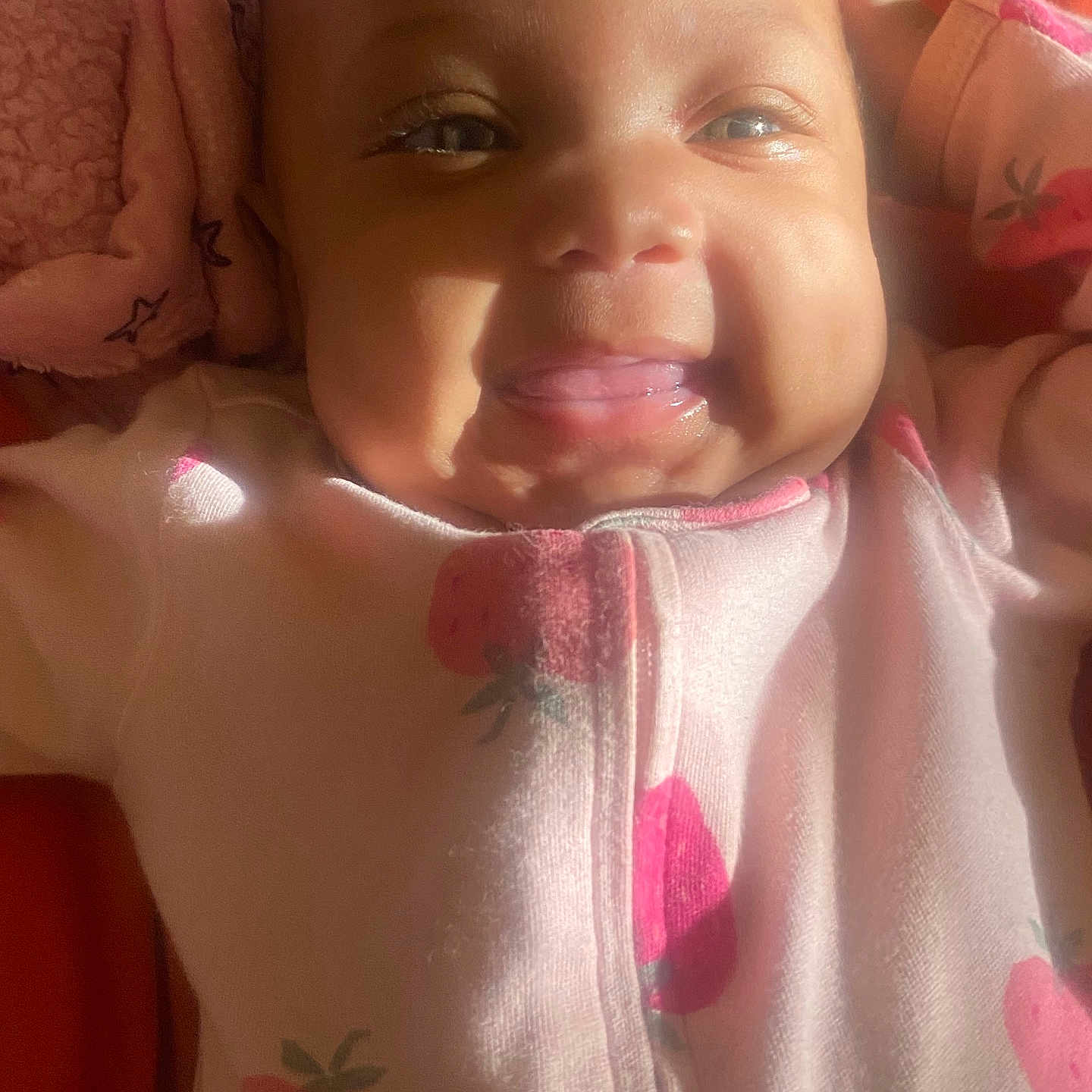 Jaliyah Aka Cookie joined the competition — help win amazing prizes! baby, infant, child, portrait, smiling, happy, face, eyes, mouth, pink_clothing, strawberry_pattern, onesie, lying_down, blanket, fabric, indoor, sunlight, warm_lighting, close_up, cozy
