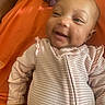 baby, infant, child, smiling, portrait, face, eyes, indoors, orange_background, baby_clothing, striped_outfit, pink, lying_down, happy, adorable, close_up, head, arms, photography, cozy