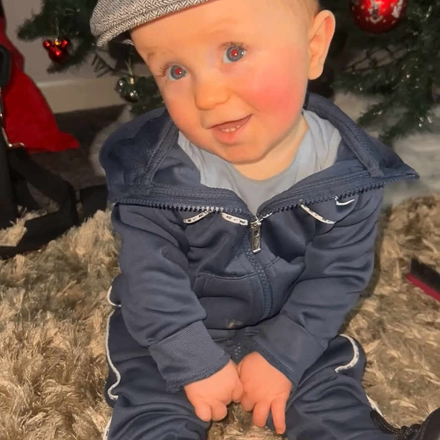 Tommy-Lee joined the competition — help win amazing prizes! baby, blue_eyes, cap, carpet, child, christmas_tree, cute, festive, hat, holiday, indoor, ornaments, portrait, red_balls, shoes, sitting, smiling, toddler, tracksuit, young