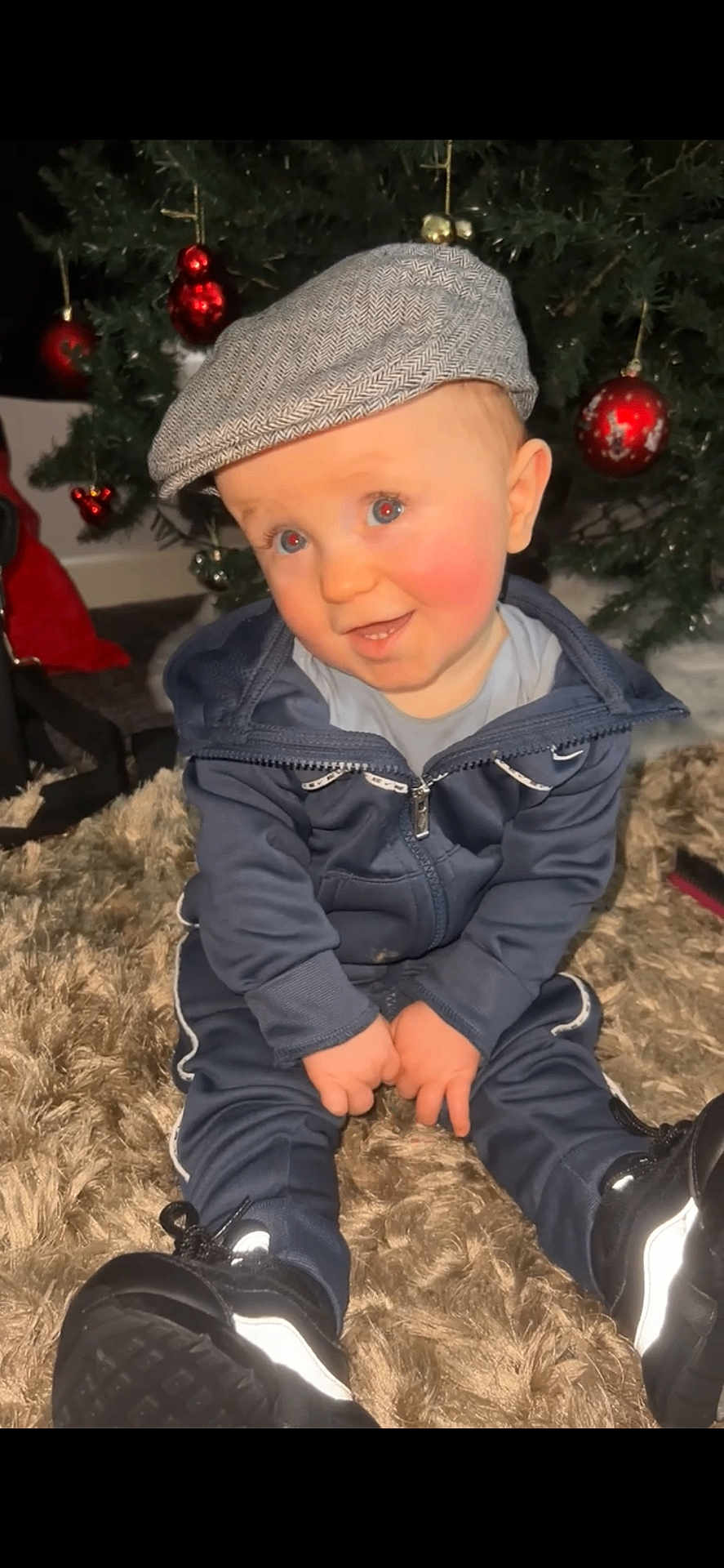 Tommy-Lee joined the competition — help win amazing prizes! toddler, child, baby, hat, cap, tracksuit, sitting, carpet, christmas_tree, ornaments, red_balls, indoor, cute, smiling, blue_eyes, shoes, holiday, festive, young, portrait