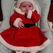 Noemie participe au concours pour gagner de l'argent avec cette photo : baby, infant, christmas, holiday, santa_outfit, red_clothing, white_trim, baby_seat, smiling, cute, cozy, indoor, plush_slippers, festive, child, portrait, happy, soft_fabric, headwear, celebration