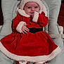 baby, infant, christmas, holiday, santa_outfit, red_clothing, white_trim, baby_seat, smiling, cute, cozy, indoor, plush_slippers, festive, child, portrait, happy, soft_fabric, headwear, celebration