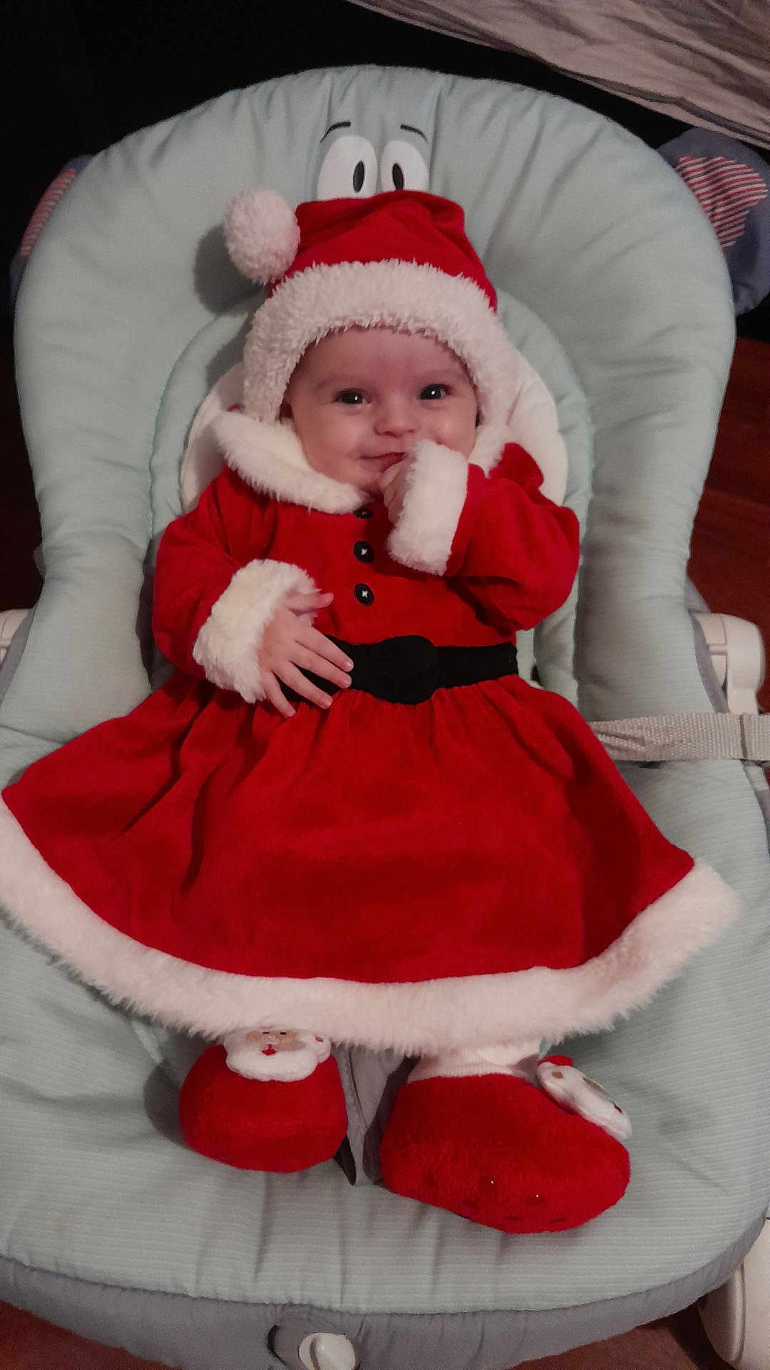 Noemie participe au concours pour gagner de l'argent avec cette photo : baby, infant, christmas, holiday, santa_outfit, red_clothing, white_trim, baby_seat, smiling, cute, cozy, indoor, plush_slippers, festive, child, portrait, happy, soft_fabric, headwear, celebration