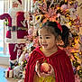 Sophia joined the competition — help win amazing prizes! child, girl, apple, red_cape, yellow_dress, christmas_tree, ornaments, lights, holiday, indoor, festive, smiling, pigtails, decorations, santa_figure, present, wood_floor, window, seasonal, celebration