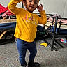 toddler, child, yellow_shirt, blue_pants, black_boots, headband, indoor, bunk_bed, carpet, clothing, person, portrait, smiling, standing, room, messy_room, furniture, earrings, cute, playful
