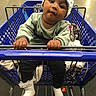baby, shopping_cart, child, hat, sweater, hands, face, store, aisle, floor, clothing, footwear, socks, curious, indoor, person, shopping, retail, seat, expression