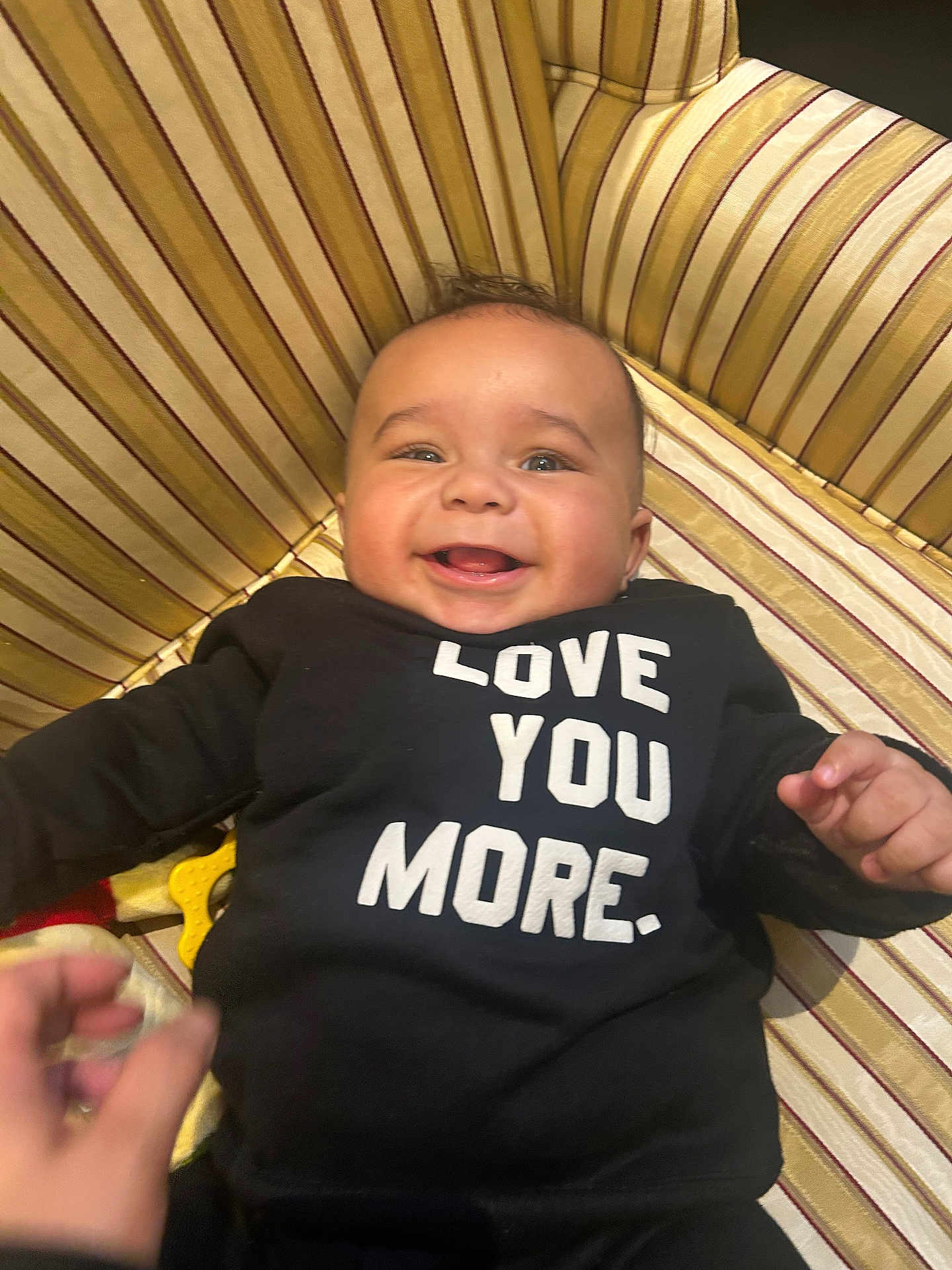 Jayce is registered to the contest to win money with this photo: baby, smiling, infant, black_clothing, text_on_clothing, striped_cushion, happy, face, hand, person, cute, child, indoors, portrait, young_child, joyful, baby_girl, baby_boy, sitting, playful