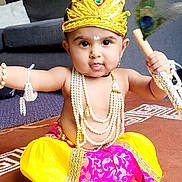 Krishnavi joined the competition — help win amazing prizes! baby, carpet, child, crown, cultural, cute, decorative, feather, footwearless, furniture, indoor, jewelry, living_room, pearls, person, playful, portrait, sitting, tongue_out, traditional_clothing