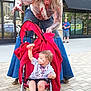 adult, barefoot, building, child, costume, face_paint, fake_blood, fruit, jeans, man, outdoor, playful, red_blanket, sidewalk, stroller, toddler, tshirt, urban, window, zombie_costume