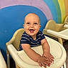 baby, high_chair, smiling, blue_shirt, striped_clothing, rainbow_wall, indoor, child, happy, seated, hands, face, head, eyes, mouth_open, furniture, colorful_background, playroom, cute, infant
