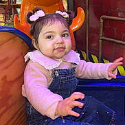 Kiana a rejoint le concours — aidez-le/la à gagner de superbes lots ! child, toddler, baby, face, smile, denim_overalls, pink_sweater, hair_buns, bow_hair, bracelet, sneakers, wooden_seat, amusement_ride, mall_interior, colorful, portrait, sitting, cute, playful, indoor