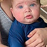 baby, child, blue_eyes, long_sleeve_shirt, curly_hair, adult_hand, striped_clothing, close_up, indoor, person, portrait, skin, expression, holding, face, young_child, cute, curious, natural_light, human