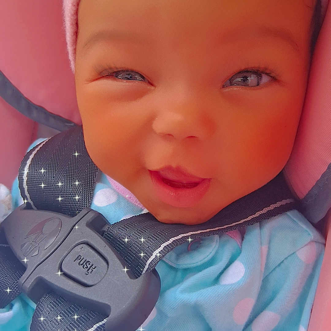 Malanii joined the competition — help win amazing prizes! baby, child, car_seat, pink_hat, blue_outfit, polka_dots, winking, smiling, cute, infant, child_seat, safety_harness, closeup, face, hand, apparel, indoors, person, young_child, adorable