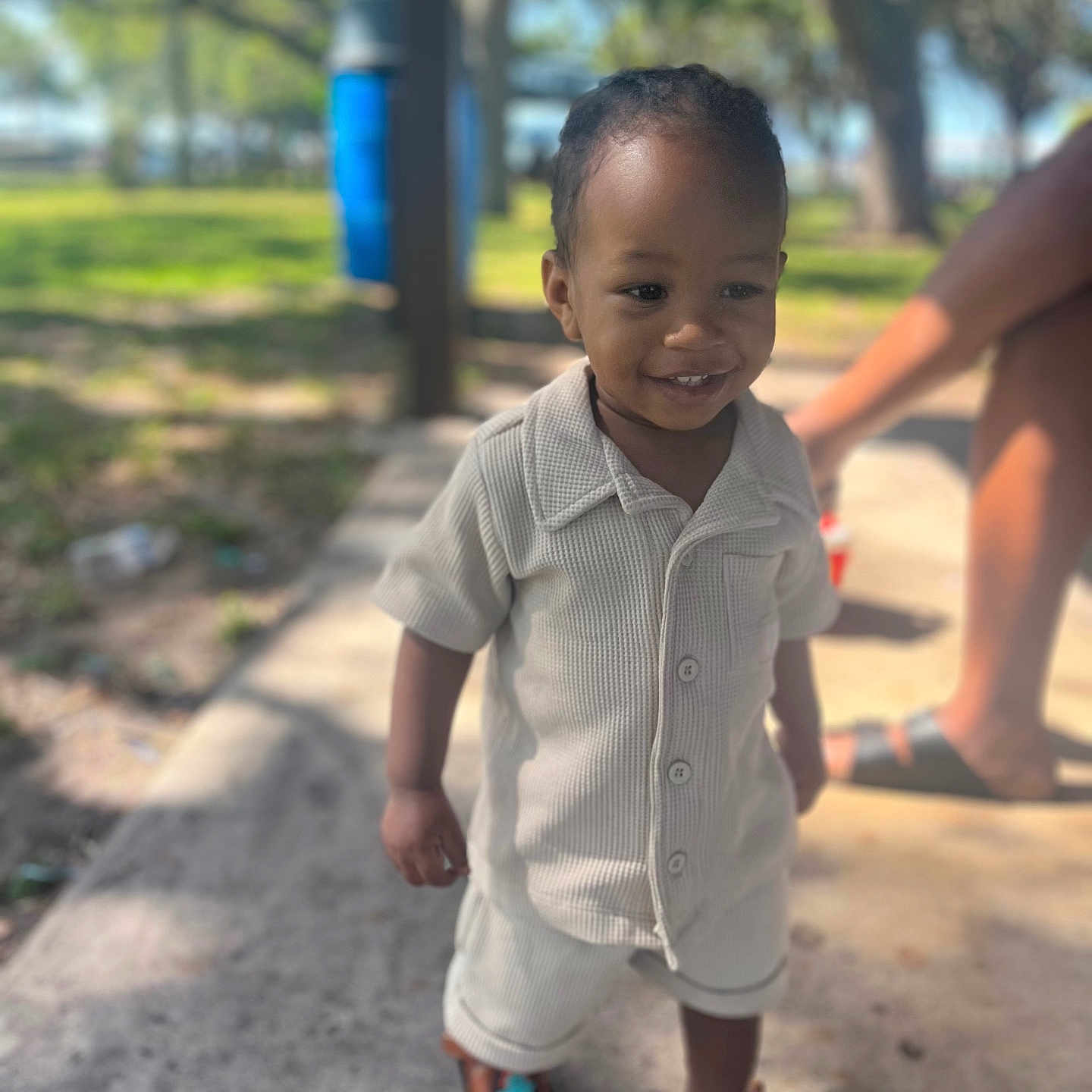 Kymire joined the competition — help win amazing prizes! blurred_background, casual, child, clothing, concrete, cute, daytime, happy, legs, outdoor, park, person, sandals, shirt, shorts, smiling, sunlight, toddler, trees, young_child