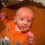 Camille participe au concours pour gagner de l'argent avec cette photo : baby, infant, pacifier, onesie, orange_clothing, dog_design, cute, lying_down, curious, soft_lighting, indoor, child, young, face, head, small_hand, texture, warm_colors, fabric, sleepwear