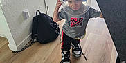 Julian is registered to the contest to win money with this photo: toddler, child, indoor, floor, bucket, shoes, sneakers, clothing, backpack, door, couch, person, hat, light, wood_floor, playful, smiling, home, curious, standing
