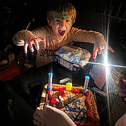 Kyson is registered to the contest to win money with this photo: child, face_paint, birthday, cookie_cake, candles, light, dark, hands, celebration, spider_man_shirt, table, party, excitement, expression, indoor, person, face, food, fun, smile