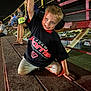 Sawyer is registered to the contest to win money with this photo: bleachers, boy, cars, child, crowd, ear_protection, event, fence, footwear, lights, metal, night, outdoor, parking_lot, people, pose, racing_shirt, shorts, smile, spectators