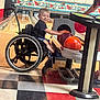 activity, adaptive_sports, bowling_alley, bowling_ball, bowling_pins, child, disability, floor_tiles, fun, game, happy, indoor, leisure, person, recreation, shorts, smiling, sports_equipment, tshirt, wheelchair