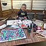 Sawyer is registered to the contest to win money with this photo: child, boy, wheelchair, painting, paint, brush, table, outdoor, fence, plant_pots, art_supplies, colorful, smiling, creative, paper_plate, clothing, tree, nature, wooden, happy