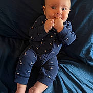 Mason is registered to the contest to win money with this photo: baby, infant, child, onesie, blue_clothing, barefoot, bed, bedroom, fingers_in_mouth, happy, cute, lying_down, skin, head, face, toes, smile, person, indoors, soft_lighting