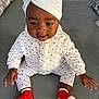 baby, infant, child, sitting, white_outfit, red_hearts, red_socks, headwrap, turban, indoor, gray_surface, cute, smiling, person, young_child, clothing, portrait, hands, feet, cozy