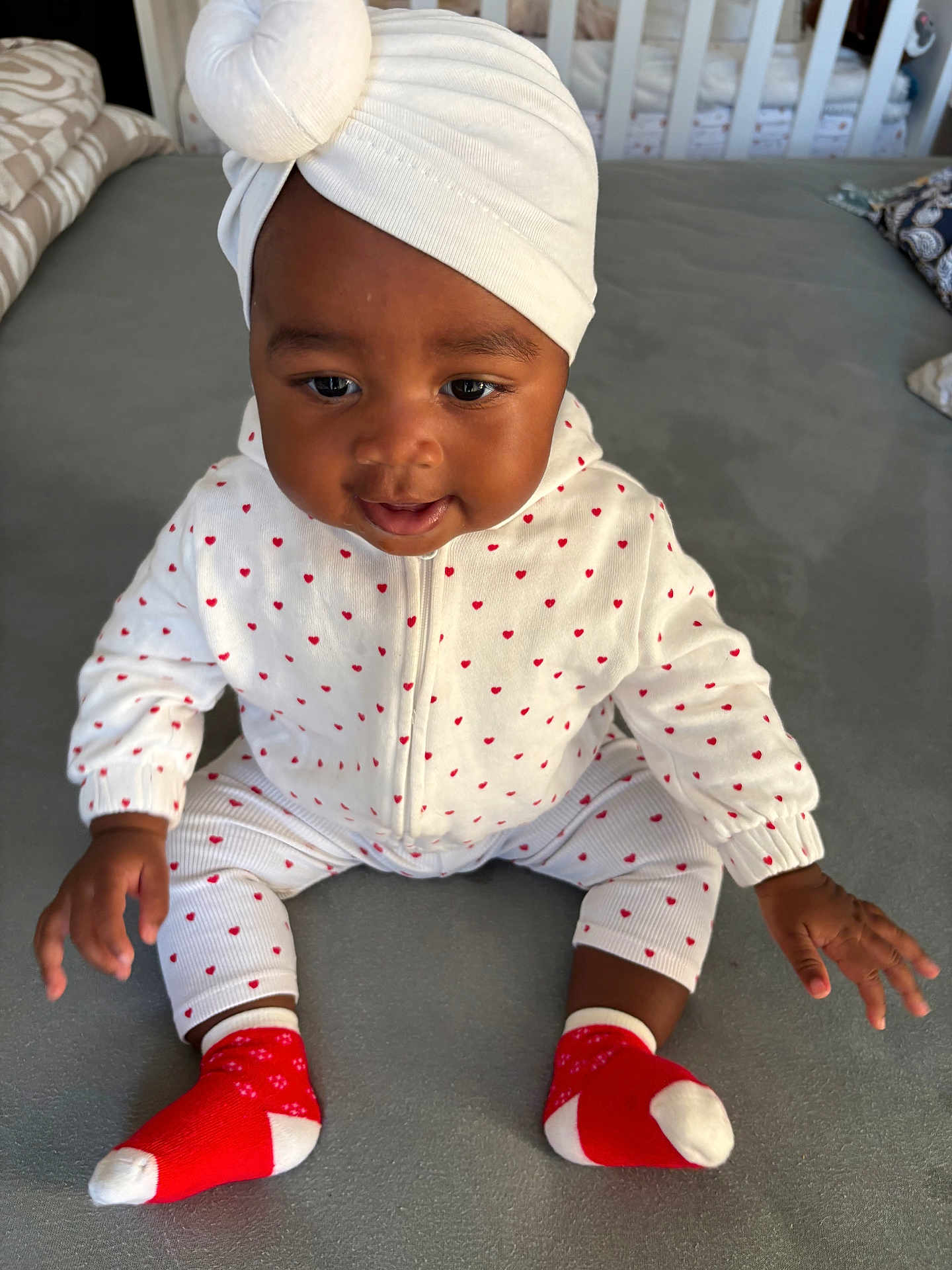 Imany participe au concours pour gagner de l'argent avec cette photo : baby, infant, child, sitting, white_outfit, red_hearts, red_socks, headwrap, turban, indoor, gray_surface, cute, smiling, person, young_child, clothing, portrait, hands, feet, cozy