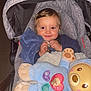 toddler, child, stroller, blanket, plush_toy, blue_clothing, smile, face, baby, cute, indoor, comfort, happy, toy, fabric, head, seat, person, cozy, infant