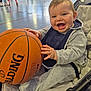 baby, basketball, casual_wear, child, clothing, cute, gymnasium, happy, happy_face, indoor, infant, joy, leisure, person, playful, seat, smiling, sports_equipment, toy, young_child