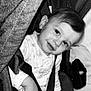 baby, child, smiling, stroller, seatbelt, black_and_white, portrait, infant, clothing, fabric, hand, face, cute, indoor, person, seat, head, young, comfort, closeup