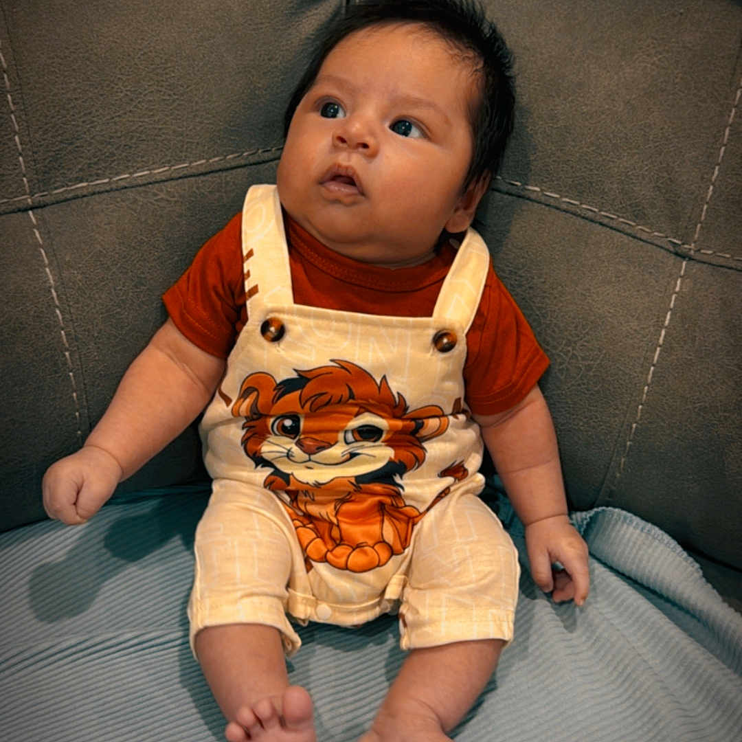 Enzo joined the competition — help win amazing prizes! baby, cartoon, child, clothing, couch, cute, eyes, fabric, face, feet, furniture, hands, indoor, infant, lion, overalls, portrait, relaxed, sitting, young