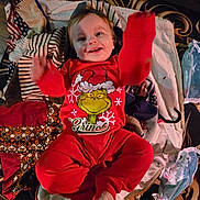 Gaberiel is registered to the contest to win money with this photo: baby, child, pajamas, red_clothing, grinch, smiling, blanket, patchwork, toy, floor, wipes, playful, happy, indoor, person, infant, cute, face, hands, feet
