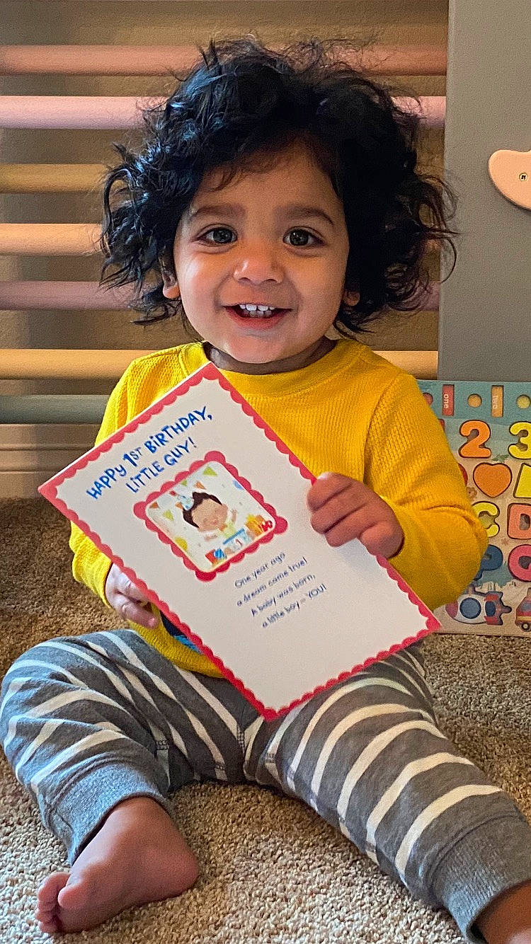 Keshav joined the competition — help win amazing prizes! adaptation, beauty, book, child, clothing, dress, facial_expression, fun, hair, hairstyle, happy, joy, person, play, reading, room, sitting, skin, sleeve, smile