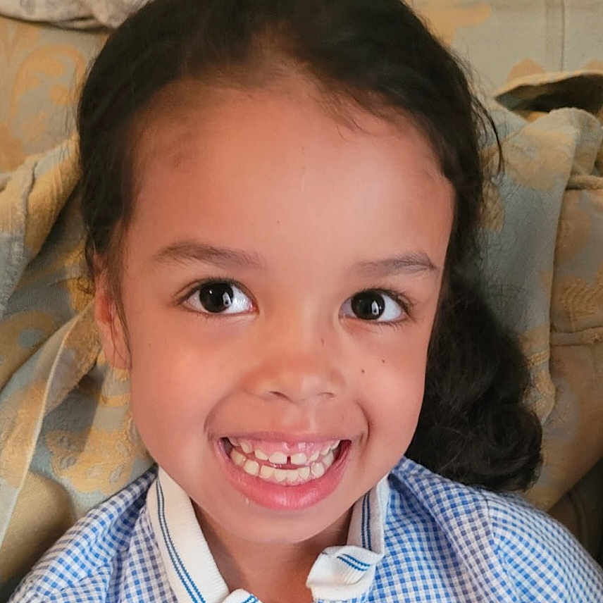 Amiyah-Jane is registered to the contest to win money with this photo: blanket, blue_checkered_shirt, casual, child, childhood, couch, cute, eyebrows, face, gap_tooth, hair, happy, indoors, person, portrait, seated, skin, smile, teeth, young