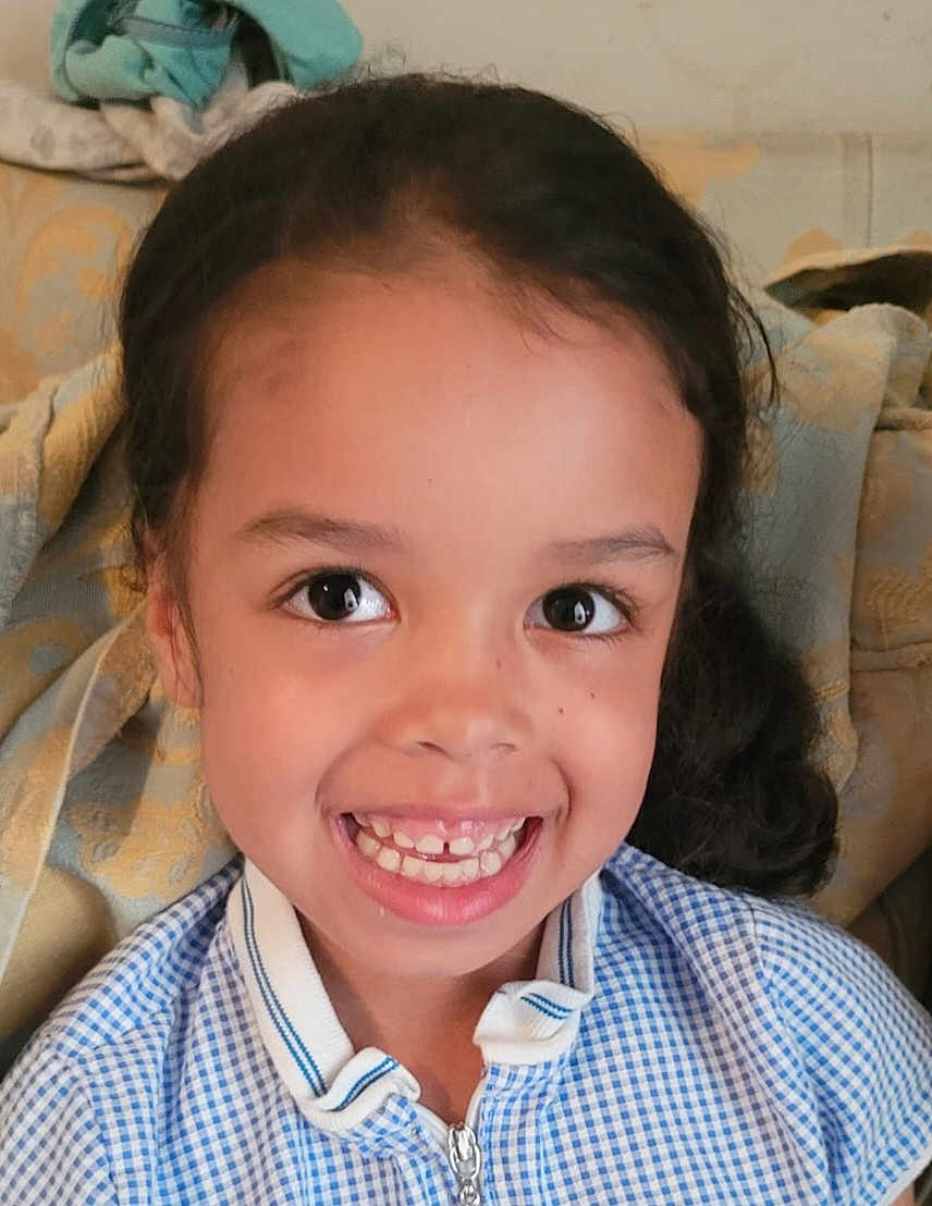 Amiyah-Jane is registered to the contest to win money with this photo: blanket, blue_checkered_shirt, casual, child, childhood, couch, cute, eyebrows, face, gap_tooth, hair, happy, indoors, person, portrait, seated, skin, smile, teeth, young