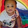 baby, brown_skin, child, close_up, clothing, colorful, curly_hair, earrings, eyes, face, indoors, looking_at_camera, minnie_mouse, play_area, play_tent, portrait, rainbow_colors, sitting, t_shirt, toddler