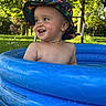 toddler, child, pool, inflatable_pool, hat, dinosaur_hat, outdoor, grass, trees, sunlight, smiling, water, summer, happy, play, nature, baby, bare_chest, blue, green
