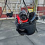 dog, puppy, swing, playground, jacket, hat, black, pet, outdoor, fence, chain, metal, seat, cute, animal, winter_clothing, park, daytime, pet_accessory, small_dog