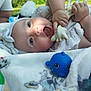 baby, child, toy, blanket, outdoor, playtime, happy, cute, infant, hand, face, headband, blue_toy, soft_toy, person, smile, skin, clothing, nature, relaxation