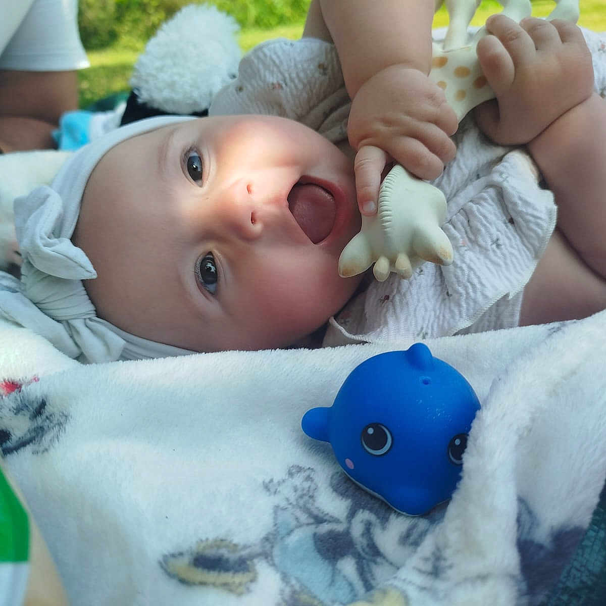 Lyana a rejoint le concours — aidez-le/la à gagner de superbes lots ! baby, blanket, blue_toy, child, clothing, cute, face, hand, happy, headband, infant, nature, outdoor, person, playtime, relaxation, skin, smile, soft_toy, toy