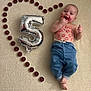 baby, infant, balloon, number_5, kiss_marks, lipstick, metallic_balloon, heart_shape, tealight_candles, carpet, blue_pants, shirtless, smiling, lying_down, celebration, milestone, skin, feet, portrait, cozy