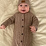 Adam-Julien a rejoint le concours — aidez-le/la à gagner de superbes lots ! baby, infant, child, knit_hat, knit_romper, blanket, bed, hands, face, eyes, smile, cozy, buttoned, texture, portrait, cute, lying_down, neutral_background, soft_lighting, beige_color