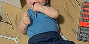 Adam-Julien a rejoint le concours — aidez-le/la à gagner de superbes lots ! baby, infant, child, lying_down, tools, wrenches, screwdriver, cardboard, stroller, wheel, license_plate, grease_smudges, blue_shirt, navy_pants, barefoot, playful_expression, surprised_face, toolbox, floor, home_workshop