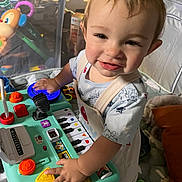 Bodhi is registered to the contest to win money with this photo: toddler, child, toy, play, keyboard, colorful, buttons, smile, indoor, cushion, clothing, person, face, hand, furniture, playpen, happy, young_child, activity, expression