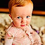 child, toddler, baby, face, blue_eyes, red_hair, floral_clothing, pink_outfit, blanket, soft_texture, indoors, portrait, curious_expression, cute, sitting, close_up, person, young_child, innocent, bright_eyes