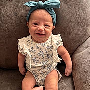 Alaynna is registered to the contest to win money with this photo: armchair, baby, bow, child, closeup, couch, eyes, face, floral_outfit, furniture, hands, happy, headband, indoor, infant, onesie, photography, portrait, sitting, smiling