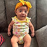 armchair, baby, child, colorful_clothing, couch, cute, front_view, furniture, headband, indoors, infant, onesie, orange_bow, photography, pineapple_pattern, portrait, sitting, smiling, textile, wide_eyed