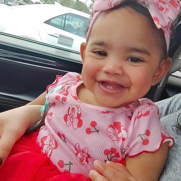 Kailani is registered to the contest to win money with this photo: toddler, child, smiling, pink_dress, headband, car_interior, happy, sitting, person, baby, cute, hand, red_skirt, window, vehicle, seat, face, portrait, clothing, accessory