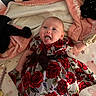 Summer is registered to the contest to win money with this photo: baby, infant, dress, red_roses, blanket, bed, clothing, tongue_out, happy, smiling, cute, soft_toys, crib, child, person, indoors, fabric, pattern, lying_down, playful